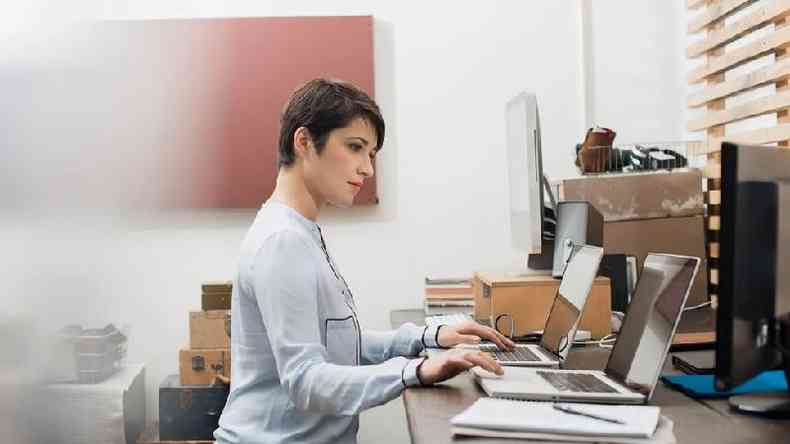 Mulher trabalhando diante de dois computadores
