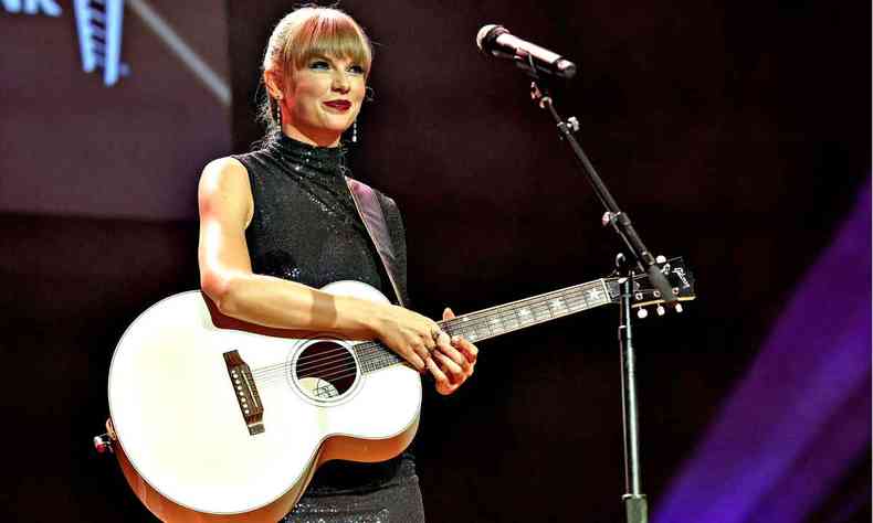 Cantora Taylor Swift est no palco e segura o violo