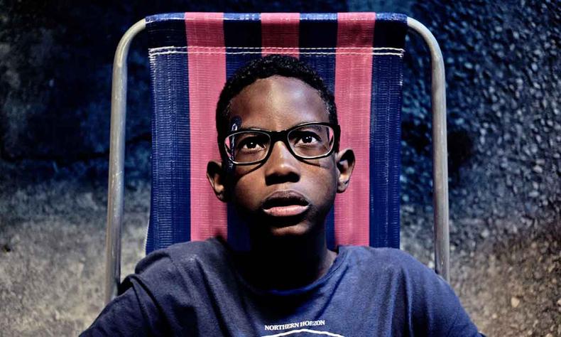 De culos, o jovem ator negro Ccero Lucas, sentado em cadeira de praia, olha intrigado para o cu, em cena do filme Marte Um 