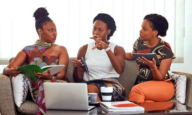 Trs mulheres negras sentadas em um sof conversando entre si com expresso sria