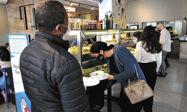 Homem observa pessoas se servindo de comida em restaurante de self service 