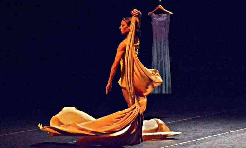 A bailarina Maria Caruso dança e segura um lençol, tendo ao fundo um cabide pendurado no cenário