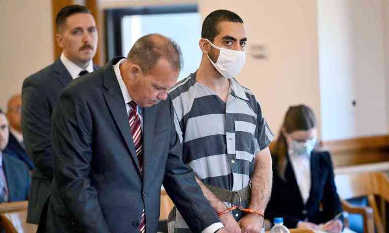 Ao lado de seu advogado, usando mscara e camisa quadriculada, algemado, Hadi Matar olha para a direo do juiz em tribunal em NY