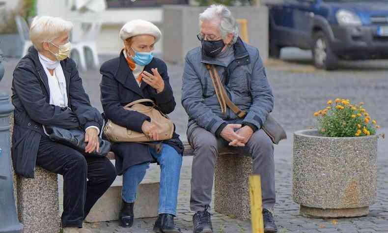 trs idosos sentado em um banco na rua, todos com mscara cotra COVID