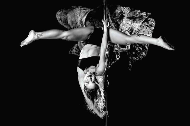 Anna Campos sorri, de cabea para baixo, ao praticar pole dance durante a pea Death Lay
