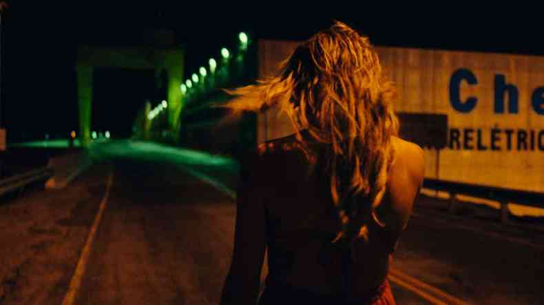 atriz de costas com longos cabelos louros em ambiente escuro em cena do filme 'Deserto particular'
