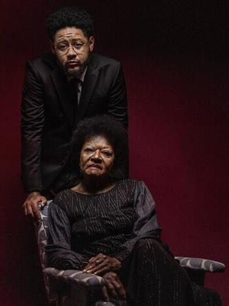 Cantora Alade Costa est sentada e o rapper Emicida est atrs da poltrona, curvado sobre ela