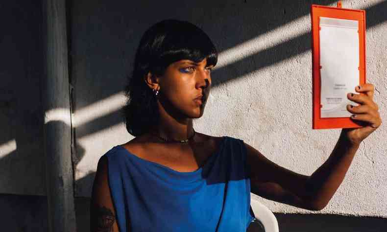A artista Laryssa Machada segurando um espelho que produz sombra em seu rosto