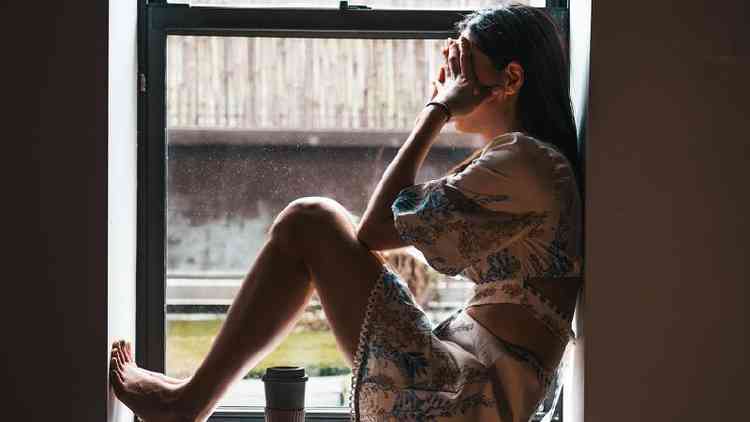 Uma mulher sozinha sentada em frente a uma janela com as mos no rosto