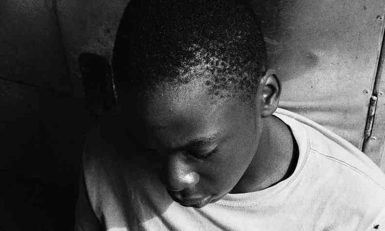 Foto de menino negro, em preto e branco, olhando para baixo 