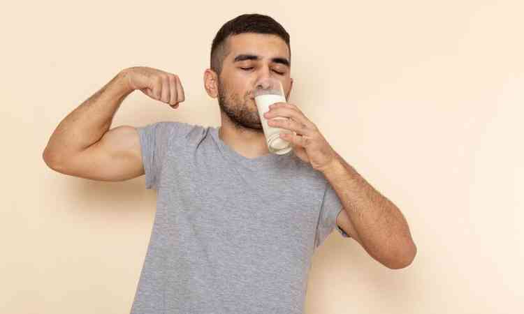 Jovem homem vestindo camiseta cinza bebendo leite bege