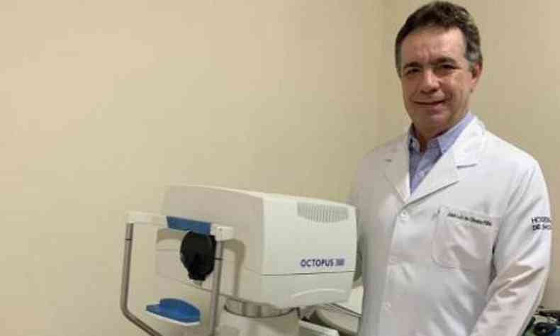 Oliveira Filho, com jaleco branco, ao lado de equipamento de oftalmologia