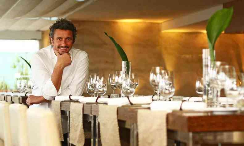Chef Emmanuel Bassoleil sorri diante de mesa de restaurante cheia de taas de cristal