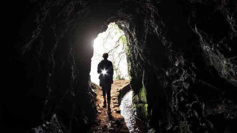 Pessoa entrando em caverna com lanterna na mo