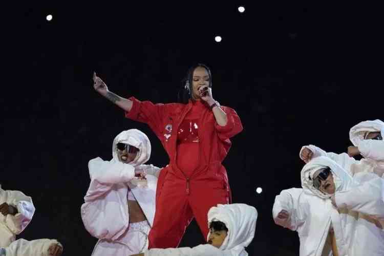 Rihanna no palco vestida de vermelho rodeada por bailarinos de branco 