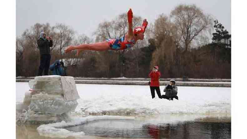 Mergulhadora pula de uma plataforma de gelo para mergulhar em um lago cercado por neve
