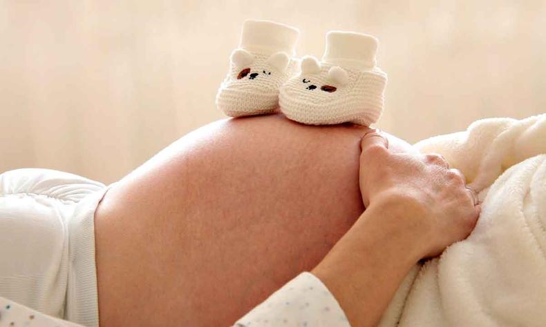 Mulher grvida deitada, com sapatinhos de beb sobre a barriga 