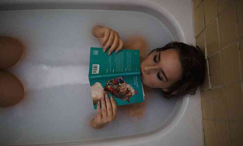 mulher na banheira relaxa lendo um livro