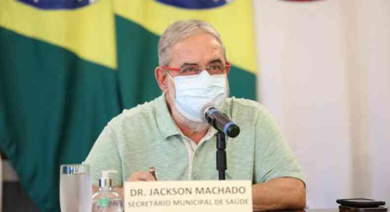 Jackson Machado durante uma coletiva com a bandeira do Brasil ao fundo