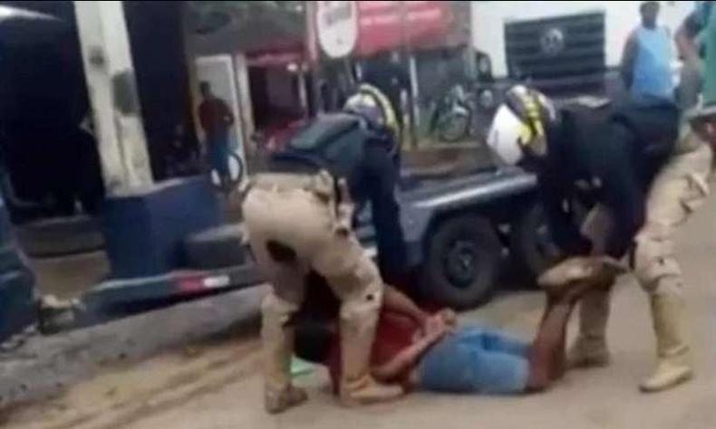 Imagem  um frame do vdeo que mostra as sucessivas agresses a Genivaldo. Dois homens uniformizados da PRF seguram o homem negro amordaado no cho