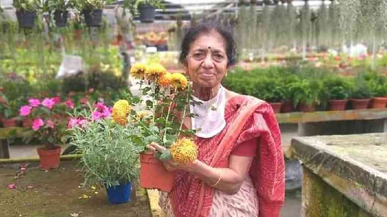 Uma senhora indiana idosa segura um vaso de flores