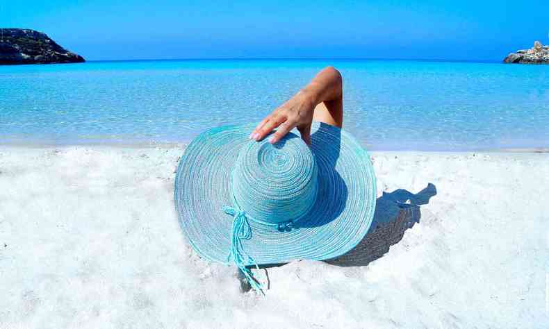 mulher na areia da praia segurando o chapu na cabea