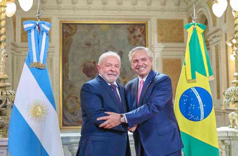 Lula e Fernndez se cumprimentam e sorriem; eles esto entre as bandeiras da Argentina e do Brasil