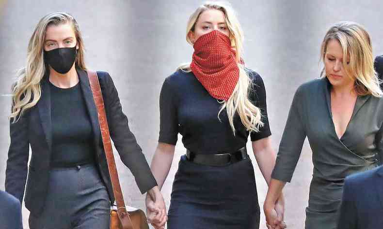 Ao lado de duas amigas, Amber Heard, de máscara, chega à corte de Londres. Todas vestem preto