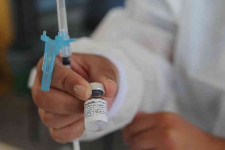 Mão segura ampola de vacina e seringa