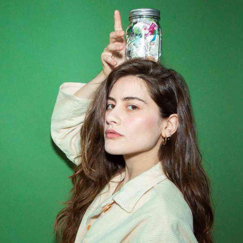 Lauren Singer em foto de estúdio, segurando um pote com resíduos em cima da cabeça