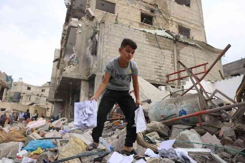 Um menino palestino procura itens recupera%u0301veis entre os escombros de um pre%u0301dio destrui%u0301do apo%u0301s os ataques ae%u0301reos israelenses noturnos em Rafah, no sul da Faixa de Gaza, em 9 de outubro de 2023