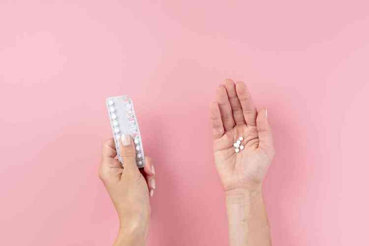 Mulher segurando anticoncepcional e pilulas sobre fundo rosa