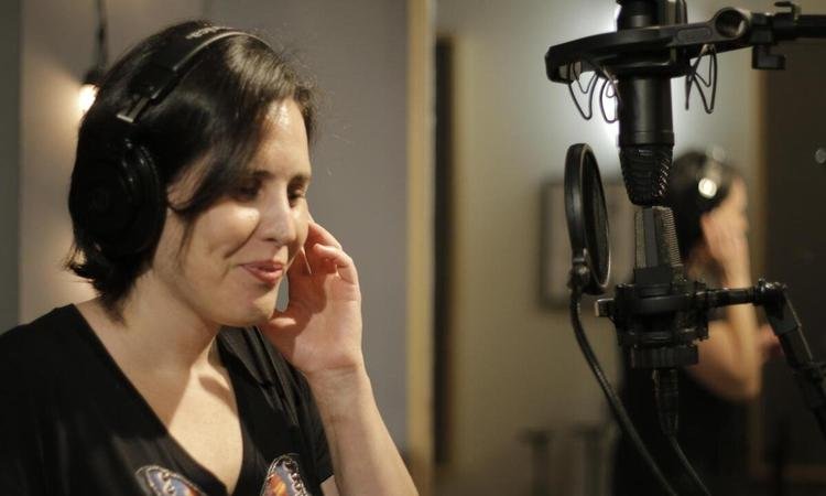 Cantora Mariana Brant, com fones de ouvido, est� ao microfone em est�dio de grava��o