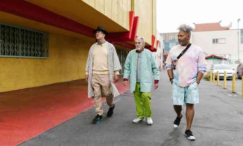 Três homens, dois brancos e um negro, acima de 50 anos andando lado a lado. Eles usam roupas consideradas modernas.
