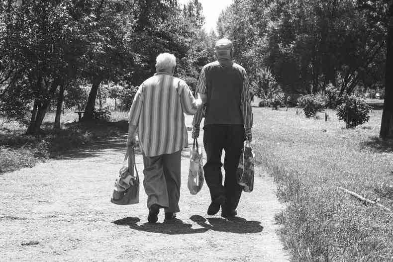 idosos caminham lado a lado em estrada segurando bolsas 