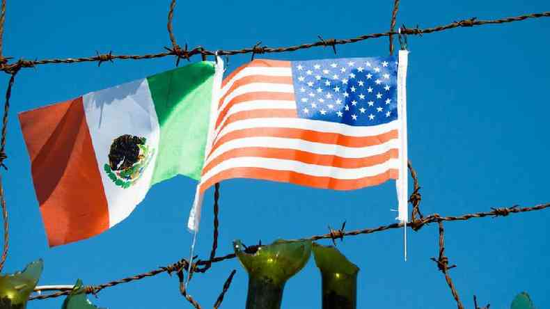 Arame farpado com bandeiras do México e dos Estados Unidos ao fundo