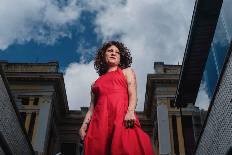 Cantora e compositora mineira marina gomes usa vestido vermelho em foto que tem o cu como fundo
