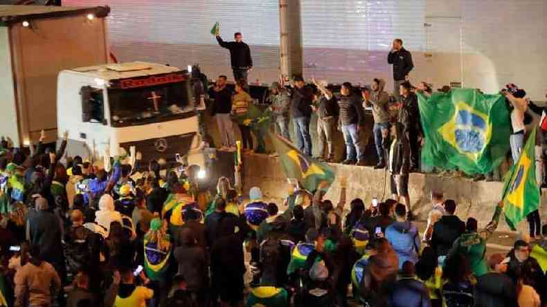 Pessoas com bandeira do Brasil acenam para caminho em rodovia ocupada