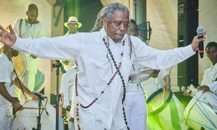 Cantor e compositor maurício tizumba usa roupa branca e de braços abertos dança durante espetáculo