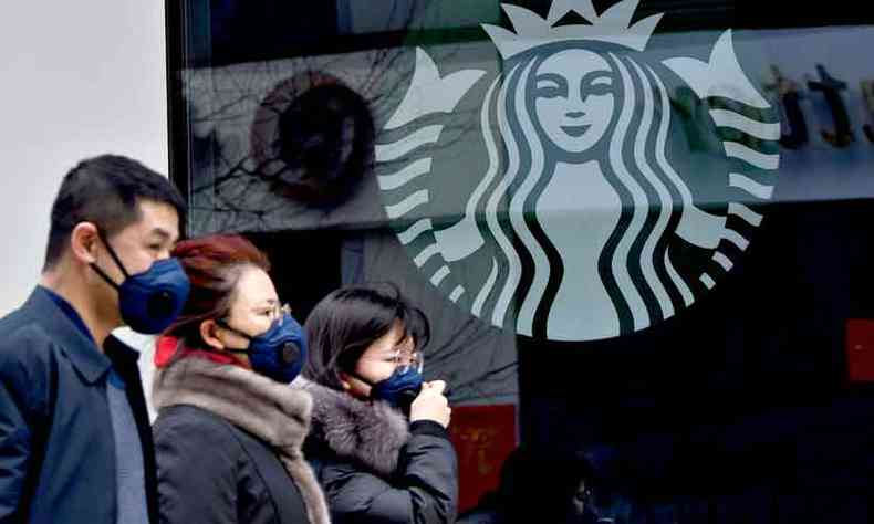 Usando mscaras, moradores de Pequim passam em frente a uma loja da Starbucks (foto: NOEL CELIS/AFP)