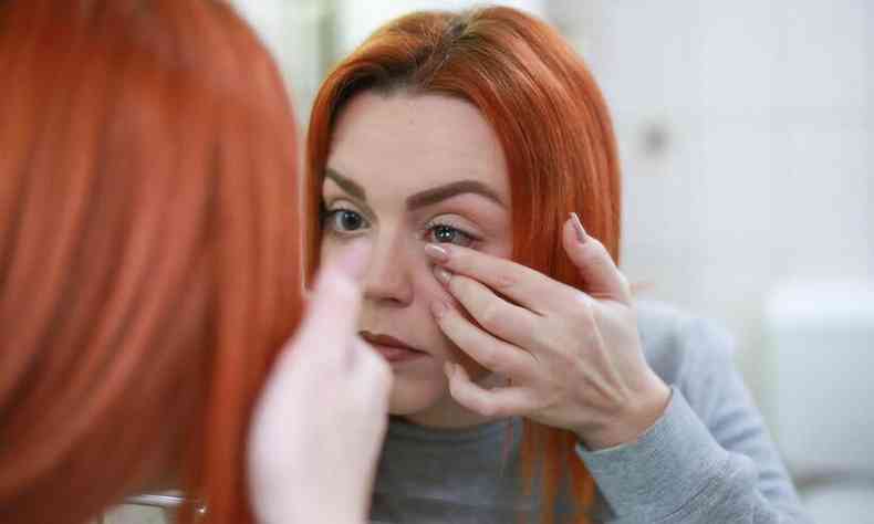 Mulher de cabelo ruivo em frente ao espelho colocando a lente de contato
