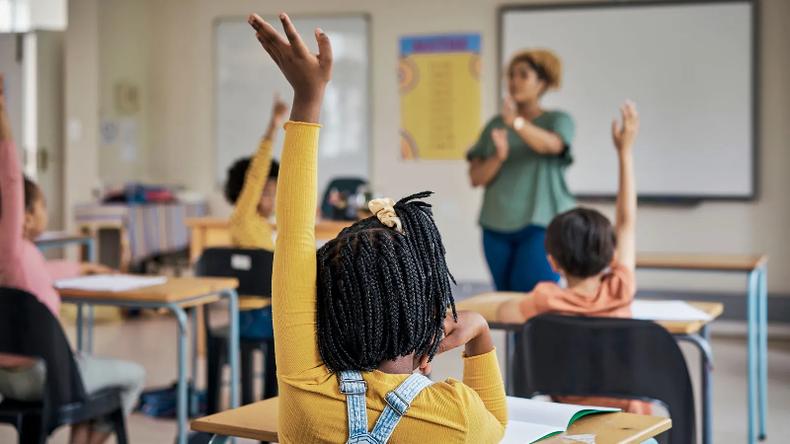 Menina negra levantando a mo esquerda em sala de aula