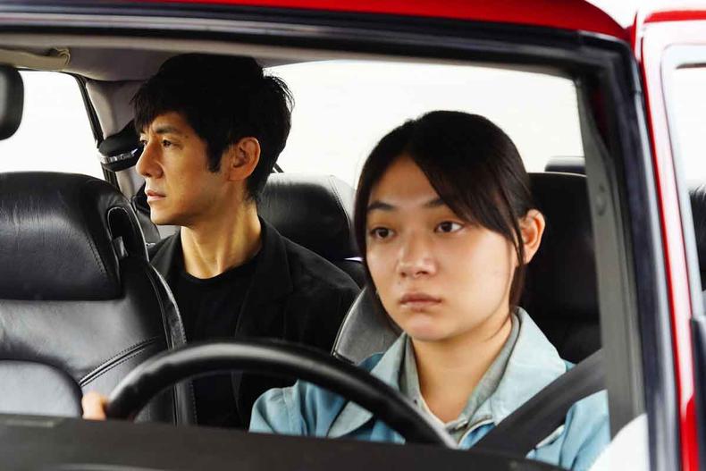 Atriz Toko Miura, sentada ao volante de carro, com cinto de segurana afivelado, olha para a frente, enquanto ator Hidetoshi Nishijima, sentado no banco de trs, olha pela janela, em cena de drive my car 