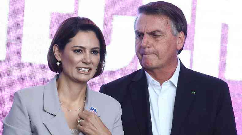 Bolsonaro olhando com feio fechada para Michelle, que sorri, em evento 