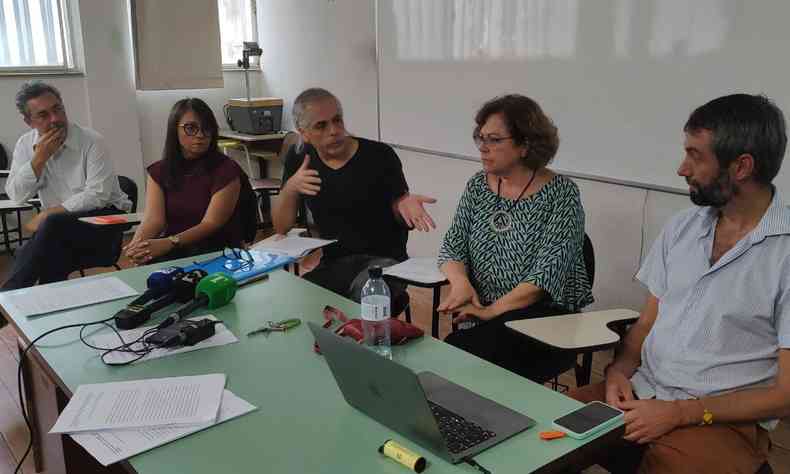Cinco pesquisadores, professores e urbanistas sentados em uma mesa de sala de aula conversando, com papeis em cima da mesa