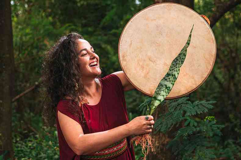 Cantora Luzmilla Luz sorri, tocando tambor, usando espada-de-so-jorge como baqueta