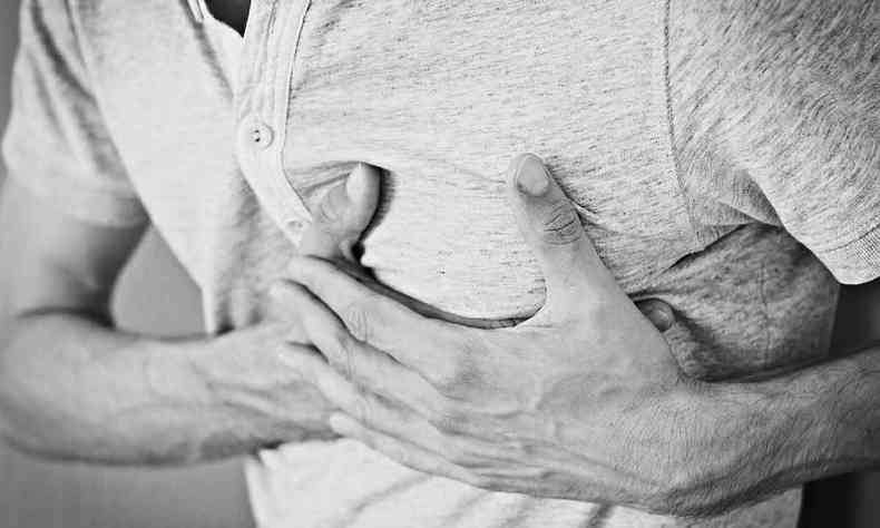 Homem leva as duas mãos ao coração, em foto que sugere dor causada por problemas cardíacos
