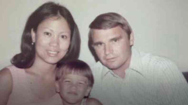 Tom Justice criança (ao centro) com sua mãe, uma mulher de olhos puxados e cabelo preto, e seu pai , um homem branco e loiro