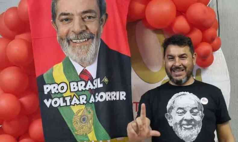 Marcelo Arruda faz L com a camisa com o rosto do ex-presidente diante de um painel com bales com Lula com a faixa presidencial
