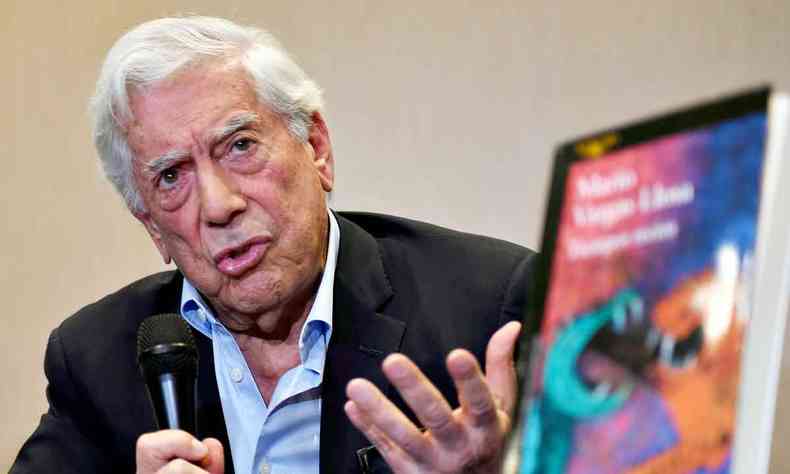 O escritor Mario Vargas Llosa fala, segurando o microfone. Na frente dele h uma tela de computador